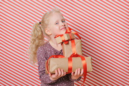 cute cheerful preschooler girl with gifts on a red striped background, gifts with a red ribbon in the hands of a girl with blond hair, boxing day, gifts for birthday and christmas, holiday giftsの写真素材