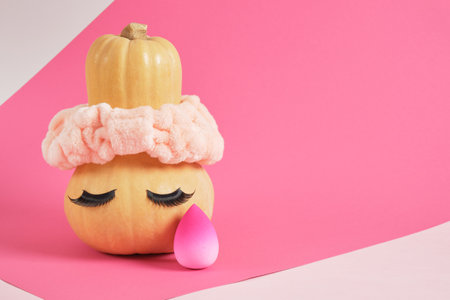pumpkin in a headband and false eyelashes on a pink background, sponges for applying makeup, makeup concept, beauty salonの写真素材