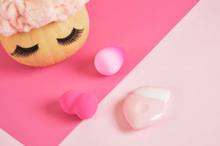 pumpkin in a headband and false eyelashes on a pink background, sponges for applying makeup, makeup concept, beauty salonの写真素材