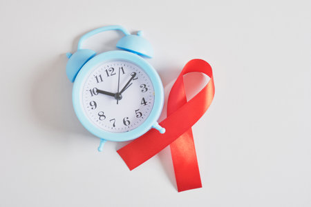 blue alarm clock and red ribbon on gray background December 1 world AIDS day copy space Healthcare and safe sex concept.の写真素材