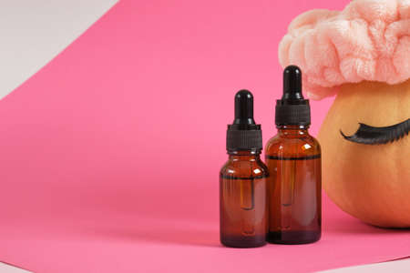 mock up set of cosmetic containers and pumpkin with headband and false eyelashes on pink background, natural skin care concept, amber glass dropper bottle for cosmetic oil or serumの写真素材