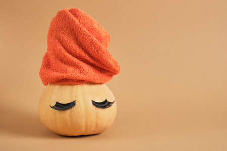 orange pumpkin with towel and false eyelashes on beige background copy space spa conceptの写真素材