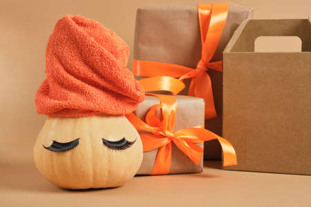pumpkin with towel and false eyelashes, gift box with ribbon and alarm clock on beige background, sale or advertising concept, christmas or thanksgiving promotion, body careの写真素材
