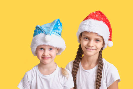 Happy smiling girls with christmas Santa hats on yellow background copy spaceの写真素材