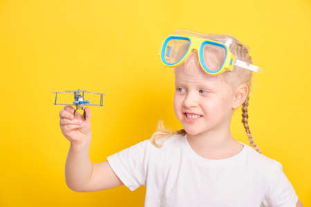 cute caucasian girl toddler with blond hair and pigtails diving mask and a toy airplane on yellow backgroundの写真素材