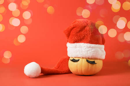 pumpkin in santa hat and false eyelashes on red background copy space