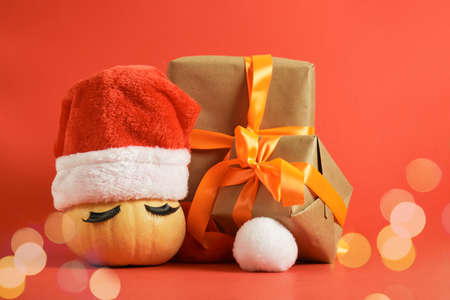 wrapped christmas gifts and pumpkin in santa hat and false eyelashes on red background copy spaceの写真素材