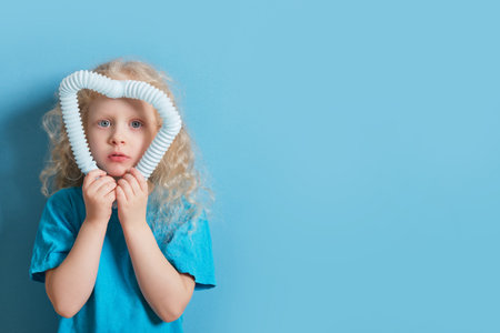 cute caucasian girl with curly blonde hair playing with pop it tube toy on blue background, trend toy for the development of fine motor skills of hands, anti stress crackling tubeの写真素材