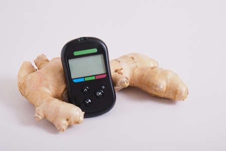 glucose meter monitor and ginger root on gray background copy space
