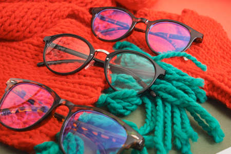 several different stylish eye glasses on a red knitted scarf, christmas sale in optics store, trendy eyeglass framesの写真素材