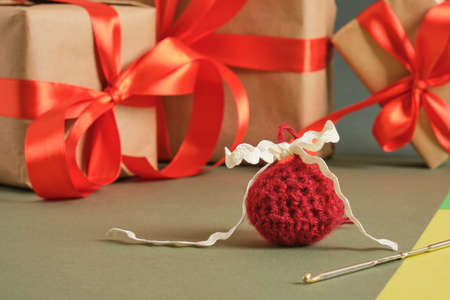 crochet hook, handmade knitted ball for christmas and gift boxes with red ribbons on a green background, craft decorations, cozy decorの写真素材