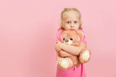 cute caucasian toddler girl hugs teddy bear on pink backgroundの写真素材