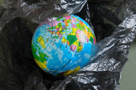 Earth tiy model in polyethylene plastic disposable package, isolated on green background. Concept pollution of environment with polyethylene plastic waste, ecological problems. Stop plastic pollutionの写真素材