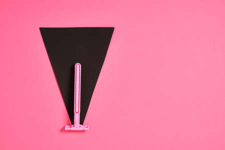 a pink plastic disposable razor and a black triangle made of paper on a pink background, an...