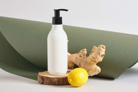 lemon, cream bottle with dispense on wooden stand and ginger root on gray and green background copy space natural cosmetic conceptの写真素材