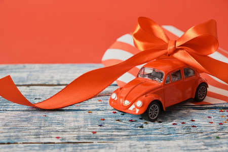 red model of a retro car on a blue wooden surface with a red ribbon bow on the roof, red background, christmas background copy space car as a giftの写真素材