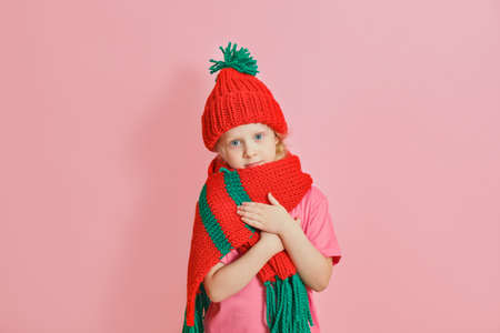 cute caucasian toddler girl in red knitted scarf and hat on pink background, christmas mood concept copy spaceの写真素材