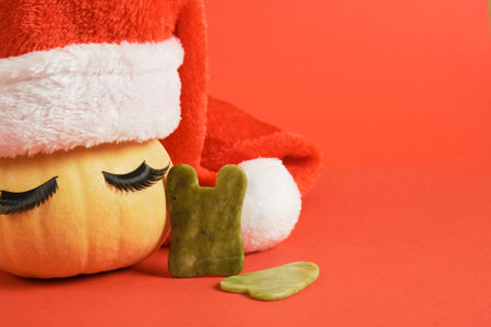 gau sha scrapers made of natural jadeite and a cute pumpkin with false eyelashes and a santa hat on a red backgroundの写真素材