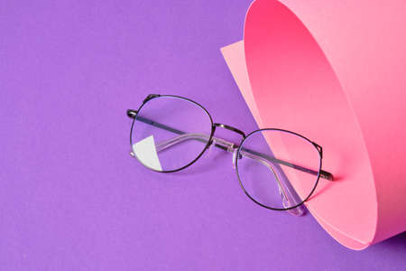 rent eyeglasses on pink and purple geometric background, trendy eyeglass frames copy space, rolled paper and fashion eye glassesの写真素材
