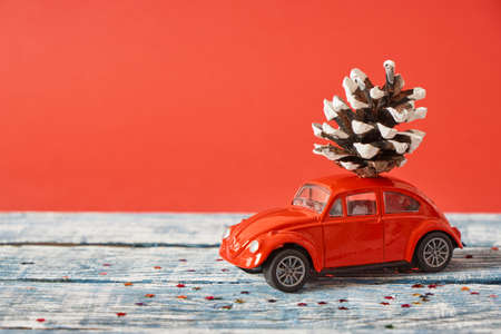 red model of a retro car on a blue wooden surface with a pine cone on the roof, red background, christmas background copy spaceの写真素材
