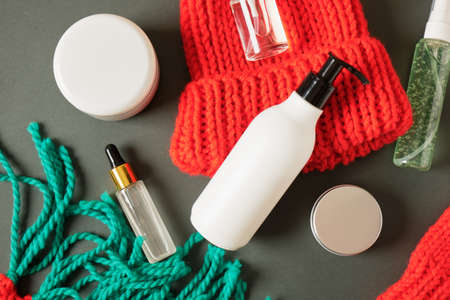 different mock up cosmetic bottles and jars and red knitted hat and scarf on green background. Christmas sale of beauty products concept. copy spaceの写真素材