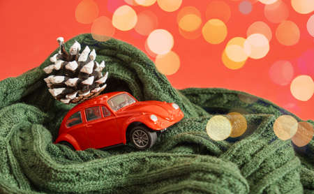 miniature purple retro car model with pine cone on the roof, little car in scarf, bokeh red nackground copy spaceの写真素材