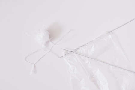Recycled plastic yarn concept, knitting needles, tangle of sliced plastic package on gray...