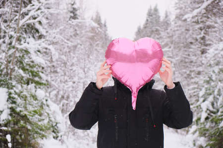 sad teen boy with pink heart shaped balloon in snowy winter forest, valentines day conceptの写真素材