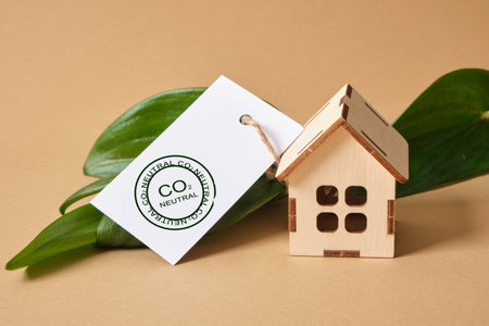 green leaves, miniature wooden house model and white tag with co2 neutral marking on brown...