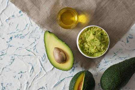 half an avocado with seed and avocado oil on a textured light background
