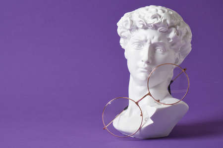 Stylish eye glasses with green frame with gypsum sculpture on a light blue background, copy space...