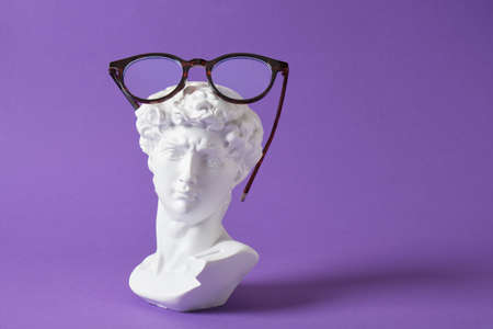 Stylish eye glasses with gypsum sculpture on a purple trendy color background, copy space David bust with eyeglassesの写真素材