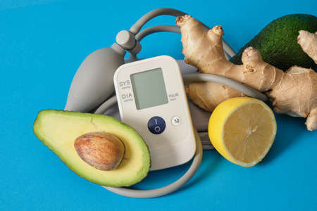 blood pressure monitor, ginger, lemon and avocado on a blue background, heart disease nutrition,...