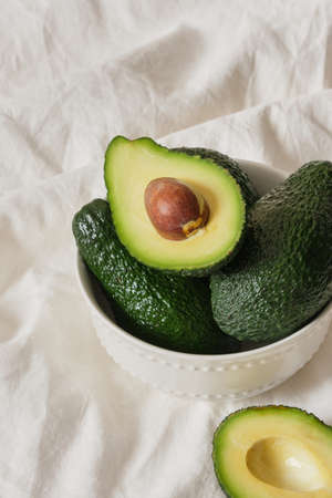 avocado in a bowl on a light texture background, sliced avocado with seeds on a white cloth, healthy breakfast conceptの写真素材