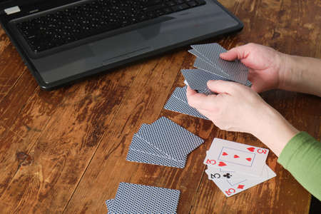 woman laying out cards for divination in front of a computer, candles, a laptop, playing cards on a...