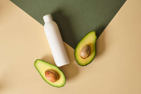mock up white plastic bottle of cream with avocado slices on a green and beige background. natural cosmetics concept.の写真素材