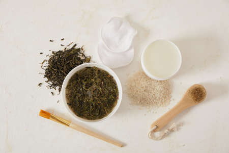 water from rice and tea for skin care in bowls, fermented cosmetics at home, natural ingredients for self-care, brush and brush for applying mask, light backgroundの写真素材