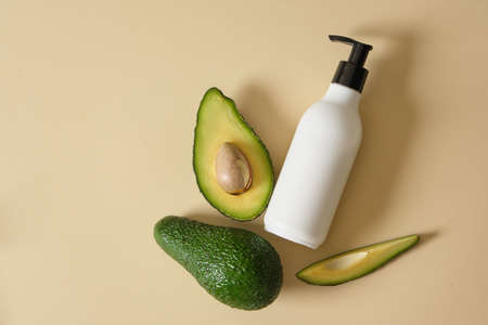 A bottle of cream with dispenser and avocado slices on a beige background. natural cosmetics concept. top viewの写真素材