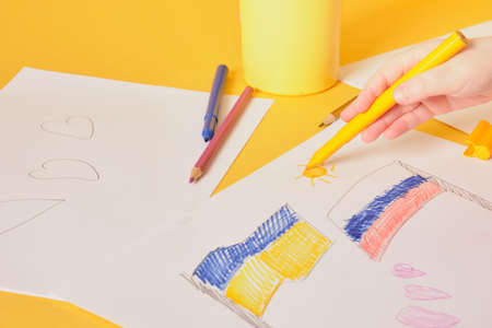 a small child draws the sun on a sheet of paper, the flags of russia and ukraine, a peaceful solution to the military conflict between countries concept, yellow background, faith in a better futureの写真素材