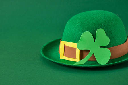 green felt hat in the style of a leprechaun and a clover leaf from foamiran on a green background,...