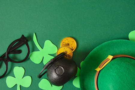 st patricks day flat lay composition, coins, felt hat, decorative clover and cauldron on green...