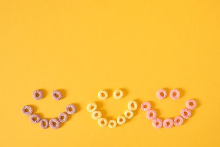 colored breakfast cereals laid out in the shape of a smiley face on a yellow background top view, childrens healthy breakfastの写真素材