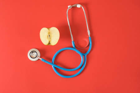 half an apple and a medical stethoscope on a bright red background, proper nutrition for diseases of the heart and respiratory tractの写真素材