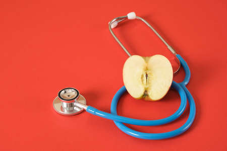 half an apple and a medical stethoscope on a bright red background, proper nutrition for diseases of the heart and respiratory tractの写真素材