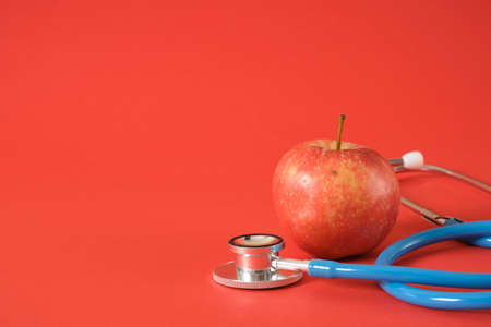 apple and medical stethoscope on a bright red background, proper nutrition and health care conceptの写真素材