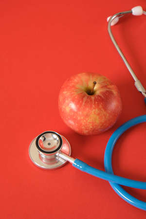 apple and medical stethoscope on a bright red background, proper nutrition and health care conceptの写真素材