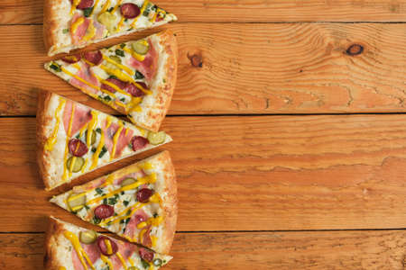 several slices of pizza with ham, sausages and pickles stacked in a row on a wooden fennel A pattern made from real pizza. top view copy spaceの写真素材