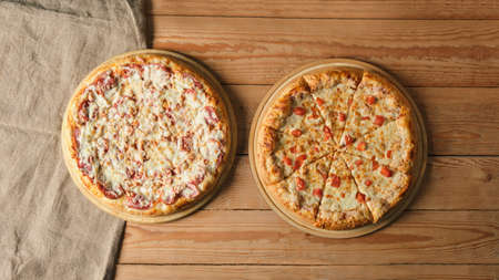 two different pizzas on a trays on a wooden background close up