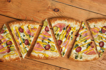 several slices of pizza with ham, sausages and pickles stacked in a row on a wooden fennel A pattern...