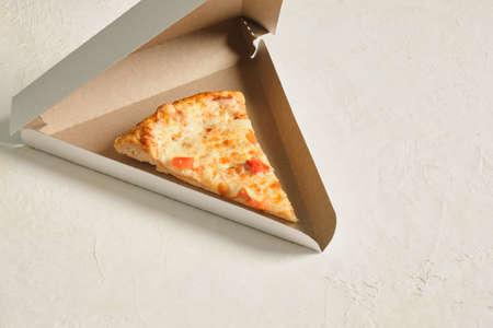 a piece of pizza in a takeaway carton box on a light background copy space
